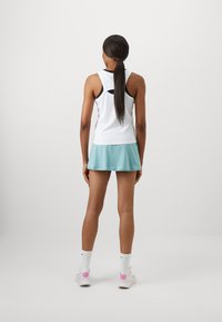 Hvit atletisk tank med svarte detaljer og åpen rygg, kombinert med en lys blå skorts. Modell iført hvite sokker og sko med rosa detaljer.