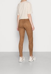 Leggings en daim marron avec une coupe ajustée, associés à un t-shirt court de couleur claire et des baskets blanches épaisses. Texture lisse sur les leggings.