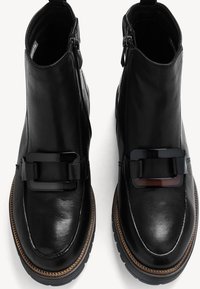 Schwarze Lederstiefeletten mit glatter Oberfläche, ausgestattet mit einer auffälligen schwarzen Schnalle und kontrastierenden braunen Nähten entlang der Sohle.