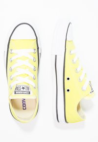 Żółte płócienne trampki z białymi sznurówkami, gumowym czubkiem i czarnymi akcentami. Posiadają oczka po bokach oraz teksturowaną podeszwę.