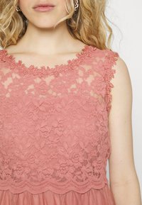 Vestido rosa con superposición de encaje floral y cuello con forma de onda. Textura suave con diseño en capas, que presenta un cuerpo transparente y una falda sólida.
