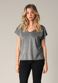 Haut gris métallisé à manches courtes avec un col en V, présentant une coupe légèrement ample et un éclat subtil. Associé à un pantalon noir ajusté.