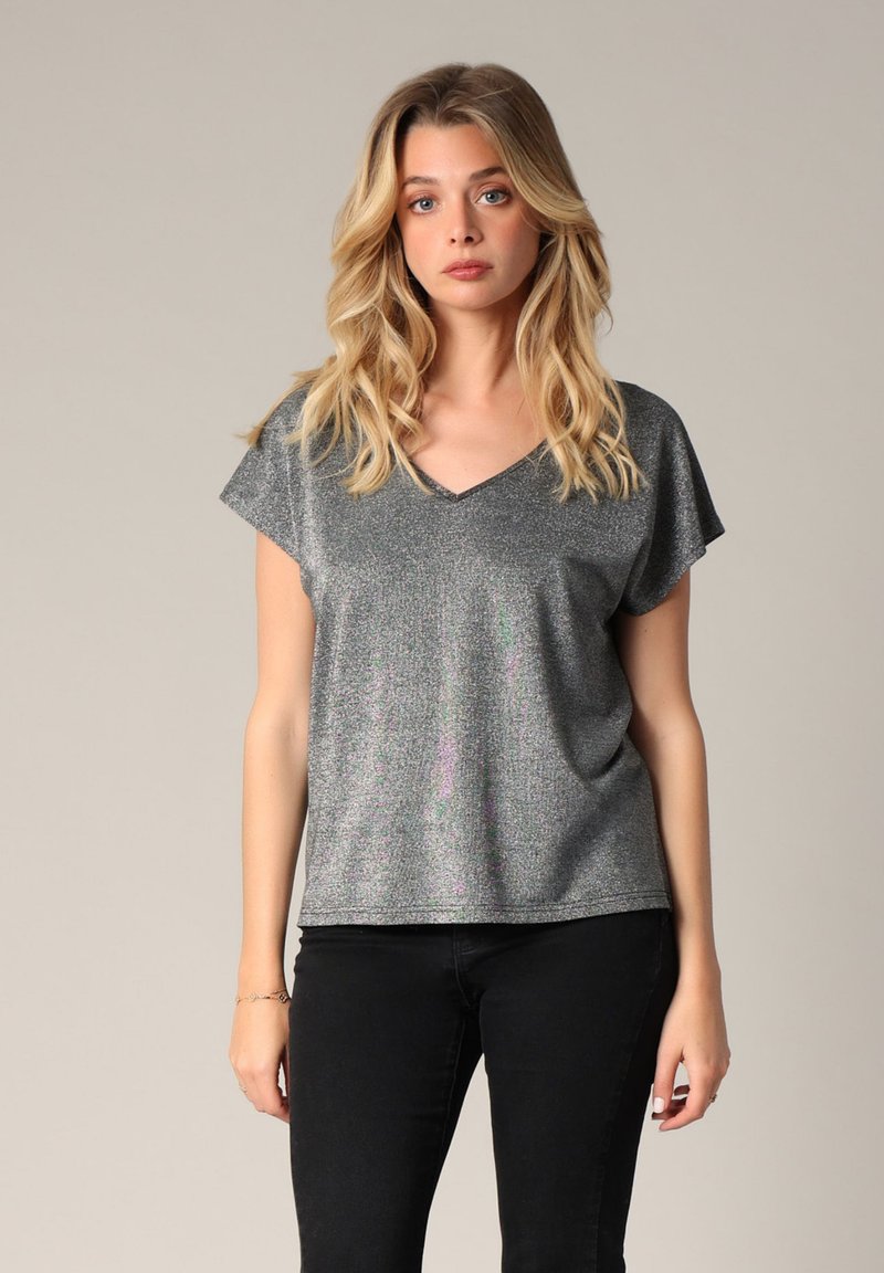 Haut gris métallisé à manches courtes avec un col en V, présentant une coupe légèrement ample et un éclat subtil. Associé à un pantalon noir ajusté.