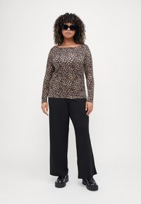 Leopárdmintás, hosszú ujjú felső, fekete, bő lábú nadrággal párosítva. A modellen fekete oversized napszemüveg és fekete magassarkú cipő található.