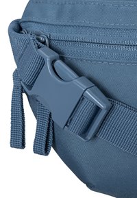Kék textúrált külsővel rendelkező anyagtasak, műanyag csattal és állítható pánttal a biztonságos záródás érdekében. Cipzár részlet látható.
