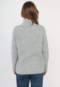 Pull en maille côtelée gris avec un col haut, offrant une coupe ample, des manches longues et une texture douce. Détails de couture visibles sur les épaules.