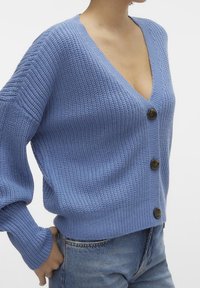 Niebieski dziergany kardigan z głębokim dekoltem w serek, długimi rękawami i trzema guziczkami. Materiał prążkowany, o luźnym kroju.
