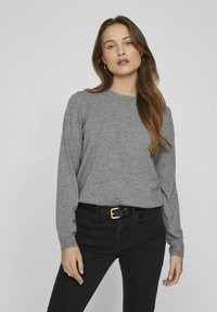 Pilkas ilgas rankovėmis megztinis iš minkštos medžiagos, su apvalia iškirpte ir smulkiais rankogaliais, derinamas su juodom džinsais ir juodu diržu su auksiniais detalėmis.