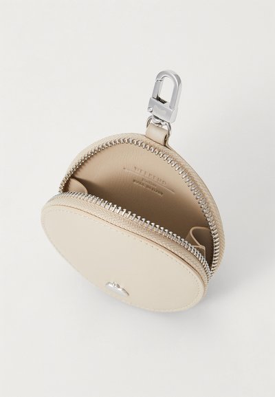 Monedero redondo de cuero beige con cremallera y clip plateados. Presenta una textura suave y un compartimento interior, con la marca grabada visible.