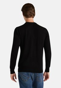 Maglione nero in tessuto a maglia liscia con scollo rotondo e maniche lunghe, abbinato a jeans blu con tasche posteriori.