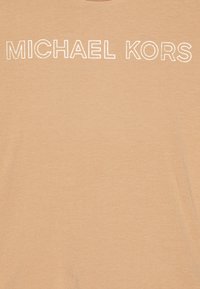 Camiseta marrón claro con cuello redondo, que presenta "MICHAEL KORS" en letras mayúsculas blancas y negritas en el pecho. Textura de tela suave.