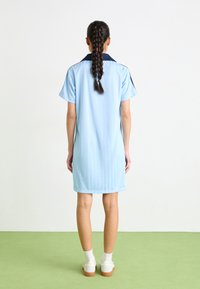 Svijetloplava kratka haljina s tamnim ovratnikom, kratkim rukavima i vertikalnim teksturnim detaljima. Bijele tenisice i čarape do gležnjeva upotpunjuju odijelo.