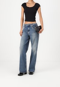 Černý žebrovaný crop top se zkosenými okraji a červenými akcenty, kombinovaný se světle modrými širokými džínami a malou černou kabelkou. Černé podpatky.