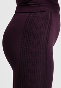 Close-up of dark purple leggings with textured chevron patterns on the side, worn with a matching high-waisted top.