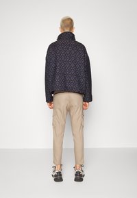 Svart och marinblå quiltad jacka med hög krage, tillsammans med beige cargobyxor och sneakers med svarta accenter. Vy bakifrån.