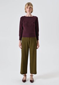 Il maglione a maglia bordeaux presenta lettere in rilievo, abbinato a pantaloni a vita alta verde oliva. Il modello indossa mocassini bordeaux in vernice.