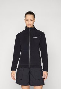 Giacca in pile nera con colletto alto e zip frontale completa. Caratterizzata da una texture morbida e abbinata a pantaloni cargo scuri.