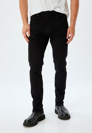 Jeans slim-fit negros de denim. Presenta un diseño de cinco bolsillos y costuras sutiles. Combinados con botas de cuero negras hasta el tobillo.
