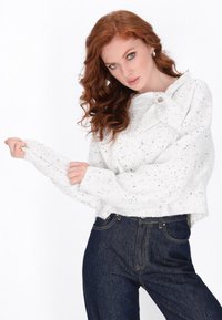 Wit gesprenkeld gebreid sweater met een ronde halslijn en strikdetail, gecombineerd met donkerdenim jeans. Sweater heeft lange, relaxte mouwen.