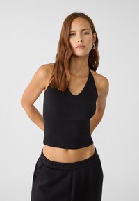 Černý crop top na ramínkách z jemného materiálu, s výstřihem do V a přiléhavým střihem, doplněný černými kalhotami se stahovací šňůrkou.