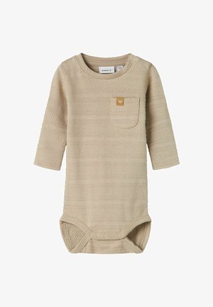 Body z długim rękawem w jasnym beżu, z teksturowanej tkaniny w poziome pasy, z małą kieszonką na piersi i zapięciem na napy na dole.