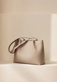 Sac cabas en cuir beige avec une finition texturée, deux longues poignées et des accents en matériel doré. Design minimaliste avec de simples détails de couture.