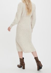 Beige stickad klänning med långa ärmar och en medellång silhuett. Kombinerad med bruna, texturerade höga stövlar med anklar.