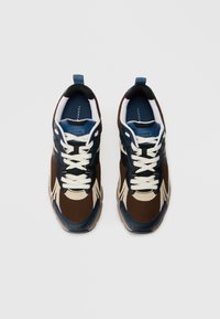Καφέ και ναυτικό μπλε αθλητικά παπούτσια με πλέγμα και συνθετικά υλικά, διαθέτοντας σχέδιο με κορδόνια, αντίθετες λεπτομέρειες και υφή στη σόλα.