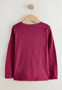 T-shirt a maniche lunghe in cotone bordeaux profondo, con vestibilità rilassata, scollo rotondo e texture liscia, appeso a una gruccia di legno.