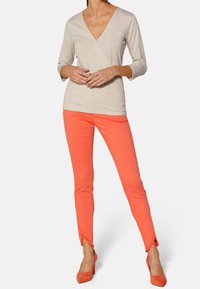 Jasnoszara bluzka typu wrap z rękawami o długości trzech ćwierć, w połączeniu z jaskrawoczerwonymi spodniami slim fit z postrzępionymi mankietami i pasującymi szpilkami.