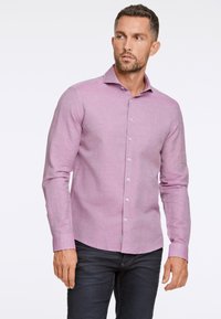 Jasnoróżowa koszula z długim rękawem, wykonana z tkanej tkaniny, z kołnierzykiem zapinanym na guziki, z białymi guzikami i slim fit. Widoczna para ciemnych dżinsów.