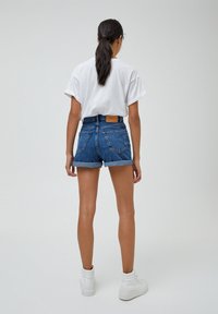 Pantalones cortos de mezclilla de cintura alta con dobladillos enrollados, de color azul, con bolsillos traseros, combinados con una camiseta blanca de corte holgado y zapatillas blancas de caña alta.