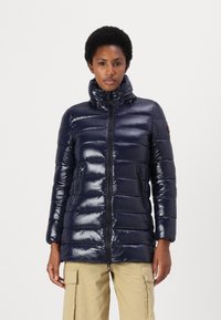 Marineblauwe pufferjack met een hoge kraag, glanzende textuur, horizontaal gewatteerd patroon, twee met rits gesloten zijzakken en een subtiele merkdetail.