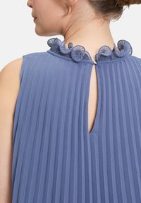 Haut sans manches bleu avec une texture plissée, col rond ornée de rosettes en tissu décoratives et une petite ouverture en forme de clé à l'arrière.