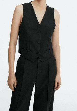 Czarna bezrękawnikowa kamizelka na guziki, zestawiona z wysokim stanem i czarnymi, eleganckimi spodniami na osobie na jednolitym tle.