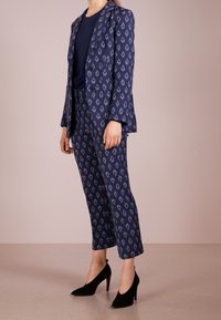 Marinblå kostym med diamantmönster, kombinerad med en marinblå topp och svarta högklackade skor. Byxorna är korta vid anklarna.
