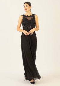 Schwarzes langes Kleid mit einem transparenten Oberteil, das mit floralen Stickereien verziert ist, fließendem Rock und rundem Ausschnitt. Weicher Stoff mit glatter Textur.