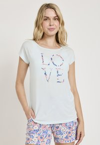 Ljusblå T-shirt med kort ärm med ordet "KÄRLEK" i blommig stil. I kombination med flerfärgade blommiga shorts med en pastellpalett.