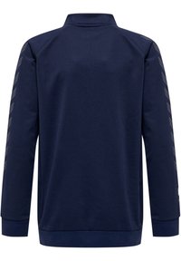 Veste zippée bleu marine en tissu lisse, dotée d'un col montant, de manches longues et de détails de design géométrique le long des manches.