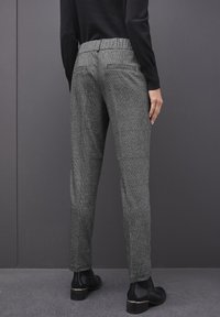 Pantalons à carreaux gris avec une silhouette ajustée, taille élastique et deux poches arrière, associés à des bottines noires.