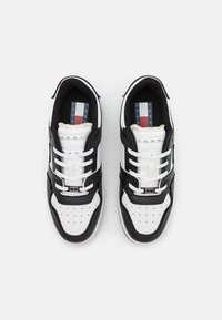 Le sneaker in bianco e nero presentano un design in pelle e tessuto, una punta perforata e il marchio "TOMMY JEAN" ben visibile sulla linguetta.