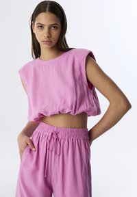 Top rosa cortado sin mangas con dobladillo recogido y diseño de hombros anchos, combinado con pantalones jogger rosa de cintura elástica a juego.