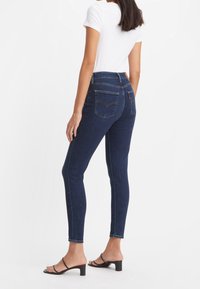 Mörkblå skinny jeans med bakfickor, hög midja och lätt stretch. Matching med en tajt vit t-shirt och svarta klacksandaler.