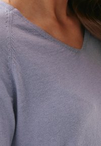 Jasnofioletowy, miękki sweter z dzianiny z dekoltem w kształcie litery V, subtelnymi detalami na ramionach, gładką teksturą i bez widocznych wzorów.