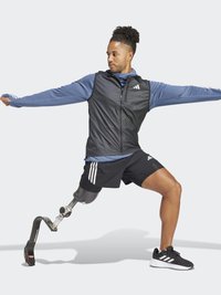Utøver iført svart vest og blå langermet skjorte med Adidas-logo, svarte shorts og svarte sko. Har en protetisk ben.