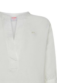 Camicia leggera bianca con scollatura a V e maniche a tre quarti. Presenta un discreto logo dorato sul lato sinistro. Tessuto strutturato.