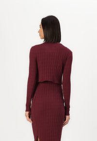 Bordo rebrasti pleteni crop top s dugim rukavima, s valovitim rubom, u kombinaciji s odgovarajućom uskom suknjom sa bočnim prorezom.