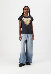 Black t-shirt with a gold feather graphic at the neckline, paired with light blue wide-leg jeans and black shoes.