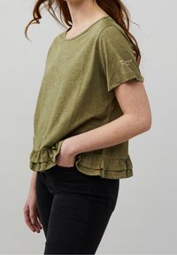 Olivgrön kortärmad topp med rund halsringning och volangans. Tillverkad av lätt material, har den en subtil textur och designdetalj på ärmen.