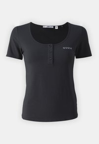 Sort t-skjorte i svart, laget av myk bomull. Har rund hals, tre-knapps placket og "GUESS"-logo i hvitt på brystet.
